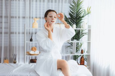 Kaplıca salonunun sakin, modern gün ışığı atmosferi, kadın müşteri poz veriyor ve yüz maskesi ile gençleştiriyor. Yüz bakımı ve güzellik kozmetolojisi prosedürü. Sessiz.