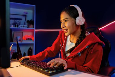 İnternet üzerinden kulaklık takıp gülümseyen Asyalı güzel kız flamasının sunucu kanalı izleyicilerle internet üzerinden konuşma yapıyor. Esport yetenekli takım oyuncuları neon mavi odada. Taktik.