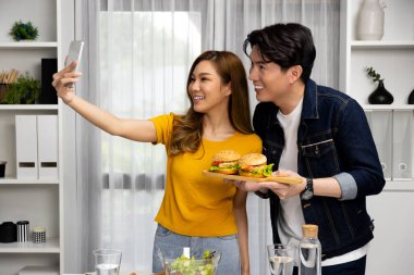 Gülümseyen sunucu şefler akıllı telefonla selfie çekerek sosyal medya kanalından canlı yayında yemek programında çift büyük hamburger yapıyorlar. İnfobahn.