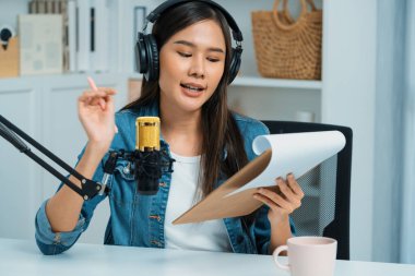 Sosyal medyada kulaklıkla canlı yayın yapan Asyalı sunucu modern stüdyoda yaşam koçluğu veya pazarlama dinleyicilerini selamlıyor. Taktik.