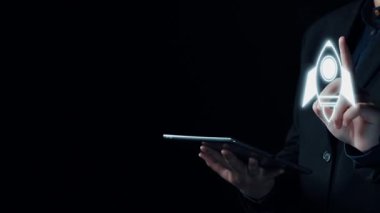 Profesyonel bir birey, iş büyümesi, yenilik ve başarıyı temsil eden çeşitli dijital sembollerle çevrili fütüristik bir roket fırlatma ikonunu elinde tutuyor. Dörtgen