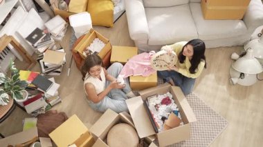 Kutuları açarken yeni eve taşınan mutlu ev arkadaşı manzarası. Çekici bir kız saati tutuyor ve arkadaşı konuşurken ve odada otururken yerleştirme pozisyonu seçiyor. Myrmidon.