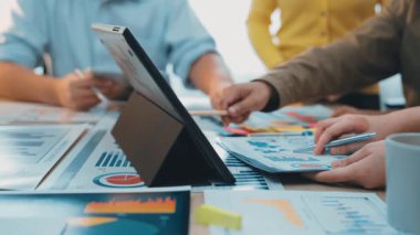 Parlak bir ofiste, etkin iletişim ve planlama için bir dizüstü bilgisayar kullanarak tablolar ve grafikleri analiz eden çeşitli bir iş adamları grubu işbirliği yapıyor. SACTR