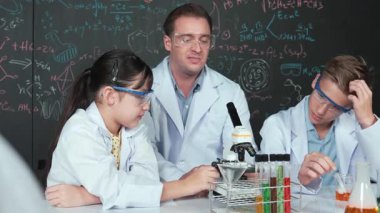 Zeki öğretmen, çeşitli öğrencilerin yaratıcı eğitim üzerine yazılmış bilim teorisiyle karatahta önünde deney yaparken test tüpü masanın üzerine yerleştirilirken mikroskop altında bakar.