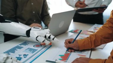 AI güdümlü asistanların pazar araştırması ve iş planlamasını geliştirdiği ve otomasyonun karar verme mekanizmasındaki artan rolünü gösteren gelecekçi bir ofis ortamı. Noogenesis Yapay Zeka