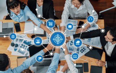 Veri tabloları ve iletişim simgeleriyle çevrili çeşitli profesyonellerin dijital ağ oluşturma ve strateji planlaması yaptığı işbirlikçi bir iş toplantısının tepeden tırnağa bir görüntüsü. Dostluk