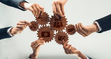 Takım çalışmasının dinamik bir temsili, sosyal medya ve etkili dijital iletişim stratejileri arasındaki bağlantıyı sembolize eden dişliler üzerinde işbirliği içinde çalışan ellerini gösteriyor. Dostluk
