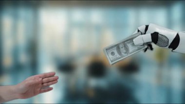 Modern ofis ortamında teknoloji ve finansmanın birleştirilmesini temsil eden, bir dolarlık banknotu insan eline aktaran bir robot elin yakın plan görüntüsü. MZL