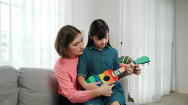 Kafkasyalı bir anne evde akustik müzik öğretirken ukulele çalan mutlu kız. Sevimli çocuk enstrüman öğreniyor. Kafkasyalı mutlu anne ve kız birlikte vakit geçiriyorlar. Pedagoji.