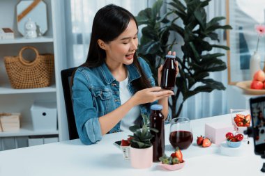 Gülümseyen, güzel Asyalı genç, lezzetli karışık çilek ve kiraz suyu detoksu içeceklerini inceleyen, sosyal medyada özel promosyon satışı için sağlıklı ürünler sergileyen. Taktik.