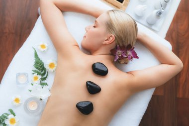 Lüks tatil köyündeki kaplıcalarda sıcak taş masajı. Gün ışığı sükunet ortamında, mutlu kadın müşteri bazalt taş masajından zevk alıyor. Rahatlatıcı bir sıcaklıkla vücudun üzerinde süzülüyor. Sessiz.