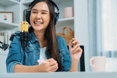 Sosyal medyada kulaklıkla canlı yayın yapan Asyalı sunucu modern stüdyoda yaşam koçluğu veya pazarlama dinleyicilerini selamlıyor. Taktik.