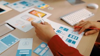 Mobil uygulama için kullanıcı arayüzü prototipini ofis çalışanlarına sunan harika bir şirket çalışanı. UX UI tasarımcısı kağıt üzerinde simge tasarımının işlevini açıklıyor. Sinerjik