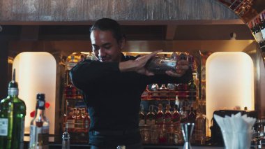 Asyalı akıllı barmen karışık kokteyl sallayarak lüks tezgah hazırlıklarına hazırlanıyor, kameranın önüne bakarak özel bir içecek hazırlıyor. Özel gece hayatı lüksü. Vinosity.