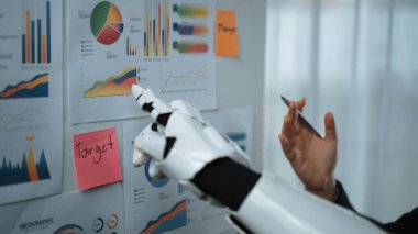 Bir robot el, modern analitik ve veri kavrayışlarını gösteren duvardaki çeşitli çizelgelerle meşgul olur. Bu görüntü teknoloji ve iş stratejisinin birleşimini temsil ediyor. Noogenesis