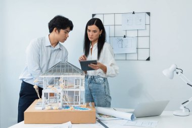Güzel, genç, beyaz bir proje yöneticisi Asyalı mühendise, mühendislik masasında ev modelini ölçerken tablet kullanarak bina detaylarını anlattı. Tertemiz.