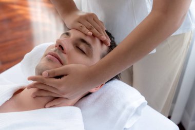 Beyaz adam stres önleyici kafa masajından ve lüks bir tatil beldesi veya otel spa salonundaki modern ışık ortamında yüz güzelliği eğlencelerini şımartmaktan hoşlanıyor. Sessiz.