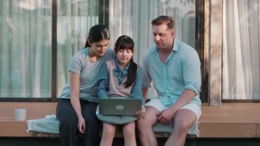 Sevimli baba, anne ve kızı birlikte evin dışındaki balkonda oturuyorlar. Ebeveynler, çevre farkındalığıyla ilgili genç nesli iletişim kurmak için açık hava aktivitelerini kullanırlar. Uyumsuzluk.