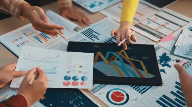 Bir grup profesyonel, tablodaki veri eğilimlerini analiz etmek, takım çalışmasını ve stratejik planlamayı geliştirmek için grafikler ve grafikler kullanarak çağdaş bir ofiste işbirliği yapmaktadır. SACTR