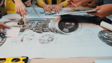 Bir grup profesyonel, bir jet motorunun teknik şemalarıyla dolu bir masanın etrafında iş birliği yapıyor. Fikirleri tartışıyor ve çeşitli bileşenleri analiz ediyorlar. SACTR