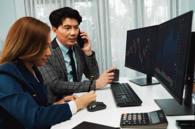 Gülümseyen Asyalı işadamı komisyoncu dinamik borsa veritabanını arıyor. Kadın iş ortağı, iç işyerindeki kar eden uygulama programını karşılaştıran ekranlara işaret ediyor. İnfobahn.