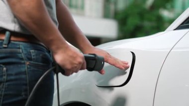 İlerici adam evindeki elektrikli aracın aküsüne emisyonsuz güç bağlantısı kuruyor. Elektrikli araç elektrik istasyonundan EV araba aküsüne kabloyla şarj oluyor.