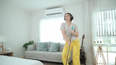 Gülümseyen kulaklıklı hizmetçi yerleri temizlerken müzik dinliyor. Oturma odasında dans ederken yerleri paspaslayan Kafkasyalı mutlu bir anne. Gülümseyen anne ev işi yapıyor. Yaşam tarzı. Pedagoji