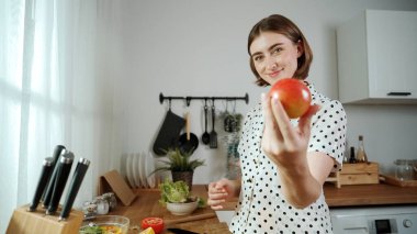Enerjik anne sağlıklı yemek yapmak ve taze elmayı tutarken kameraya bakmak için meyve seçer. Mutlu ev bakıcısı mutfakta salata hazırlarken yemek pişirmekten zevk alır. Pedagoji.