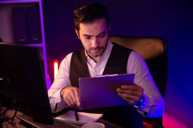 Stresli akıllı işadamı, gece geç saatlerde Mor Neon Koyu Işık Odası 'ndaki disiplin ürünleri servisinin çevrimiçi satış kanalını oluşturmak için kağıt işi raporu klasöründeki pazar verilerini analiz ediyor. Tahmin et..