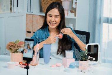 Genç, güzel Asyalı makyaj fırçası yanak testi koleksiyonunu pastel renkle inceliyor. Sosyal medyada akıllı telefonu tanıtmak için pembe ile ışıltılı bir ruh hali sergiliyor. Taktik.