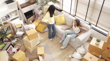 Taşındığı gün yanında oturan neşeli bir arkadaşı davet etti. Yeni evde karton kutu ve mobilyayla çevrili bir şekilde koltukta oturan mutlu bir çift kadın. Myrmidon.