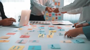 Değişik bir ekibin renkli yapışkan notlar kullanarak beyin fırtınası yaptığı, yaratıcılığı ve bir dizüstü bilgisayarın etrafındaki işbirliğini teşvik ettiği dinamik ofis sahnesi. SACTR