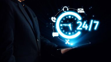 Karanlık bir arkaplanda elinde parlak bir saat gösteren bir tablet bulunan bir işadamı, dijital iletişim ve profesyonel hizmet için 24 saat kullanılabilirliği vurguluyor. Dörtgen