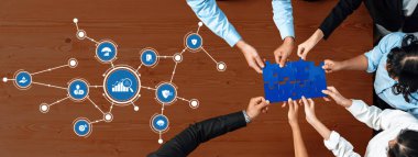 Çeşitli bir ekip, grafikler ve simgeler tarafından temsil edilen verileri analiz ederken, stratejik yönetimi ve iş dünyasındaki yenilikçi problem çözmeyi sembolize ederken bir bulmaca üzerinde işbirliği yapıyor. Dostluk