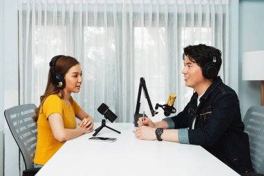 Gülümseyen radyo etkili sunucusu kulaklık takıyor kadın konuşmacı ile röportaj yapıyor sosyal medya internet sitesinden dinleyicilere bilgi paylaşıyor stüdyo kaydında sabah canlı yayın kanalı. İnfobahn.