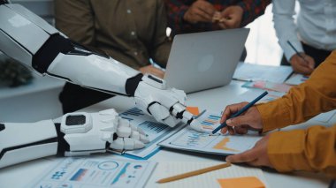 Modern bir ofiste insanlar ve bir robot arasındaki işbirliğini gösteren, tabletler ve dizüstü bilgisayarlar üzerindeki verileri analiz eden, yenilik ve takım çalışması sergileyen fütüristik bir sahne.