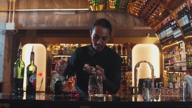 Güzel görünümlü Asyalı barmen içki şurubunu kullanarak lüks içki tezgahında cam hazırlama, gece kulübü lüksündeki düzgün profesyonel barmen kostümü yapıyor. Vinosity.