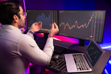 Akıllı tüccar işadamı, karanlık oda gecesinde neon ışıklı ofisteki arama pazarında yüksek kârla ekranda bilgisayar ve bilgisayar üzerinde dinamik borsa yatırımları üzerinde yoğunlaşıyor. Tahmin et..