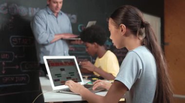 Afrikalı erkek manken tamir ederken beyaz kız programlama ya da kodlama sistemi. Öğretmen elinde dizüstü bilgisayar tutarken çeşitli çocukların web geliştirme programı yazmalarına bakıyor. Yenilik eğitimi. Öğretim