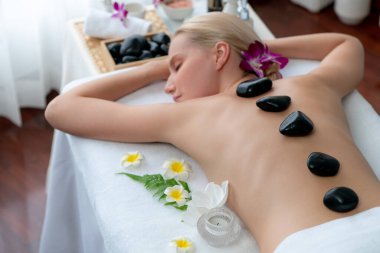 Lüks tatil köyündeki kaplıcalarda sıcak taş masajı. Gün ışığı sükunet ortamında, mutlu kadın müşteri bazalt taş masajından zevk alıyor. Rahatlatıcı bir sıcaklıkla vücudun üzerinde süzülüyor. Sessiz.