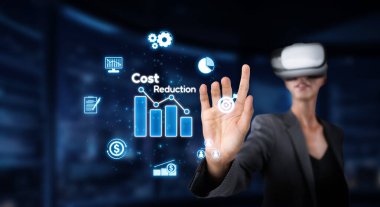 Sanal gerçeklik teknolojisini kullanan bir iş kadını, maliyet azaltma ve gider yönetimi üzerine odaklanan grafikler ve simgelerle etkileşime geçerek finansal optimizasyonu vurguluyor. XDMCP