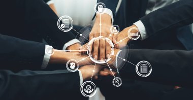 Çeşitli bir iş ekibi birlik ve ortaklığı sembolize ederek ellerini birleştiriyor. Çevrelerinde, birbirine bağlı bir dünyada büyümeyi, stratejiyi ve başarıyı temsil eden dijital simgeler bulunuyor. Dostluk