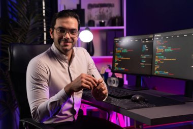 Bilgisayar ekranındaki yazılım geliştirme kodlamasına karşı poz vermek için akıllı bilişim geliştirici görünümlü kamera profilleri, neon ışıklı siber oda ofisinde program güncellemesi internet sitesi verileri sunuyor. Tahmin et..