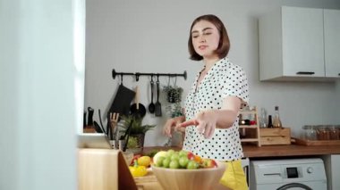 Kafkasyalı anne, modern mutfakta dizüstü bilgisayarda yemek tarifine bakarken salata yapmak için yemek hazırlıyor. Yetenekli ev bekçisi taze sebze kullanarak kahvaltı hazırlıyor. Pedagoji.