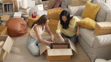 Lezbiyen aşıklar taşınma gününde karton kutudan nesneleri alıyorlar. Taşınırken paketleri açmak ve kutudan mobilya toplamak için birlikte çalışan bir çift oda arkadaşı. Yer değiştirme konsepti. Myrmidon.