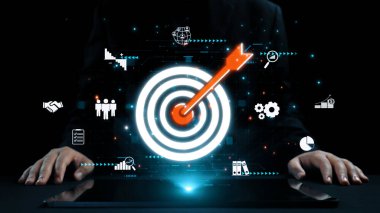 Çeşitli iş simgeleriyle çevrili dijital bir hedefin dartla vurulmasının çarpıcı görsel temsili, strateji, başarı ve yenilik temaları vurgulanıyor. Dörtgen