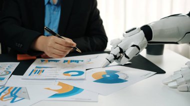 İnsan bir profesyonel, modern ofis ortamında, iş verimliliğini ve yeniliğini artırmak için veri tabloları ve raporları analiz ederek robotik bir el ile iş birliği yapar.