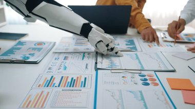 Bir robot kol, bir ofis ortamında profesyonellerden oluşan bir ekiple işbirliği yapar, tabloda gösterilen çeşitli grafik ve grafikler üzerinden verileri analiz eder.