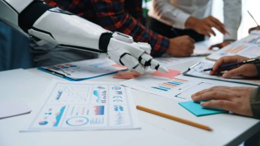 İş raporları, çizelgeler ve veriler üzerinde çalışan bir robot el ve insan eli ile dinamik ekip toplantısı ayarında ilgi çekici bir çalışma alanı. Noogenesis