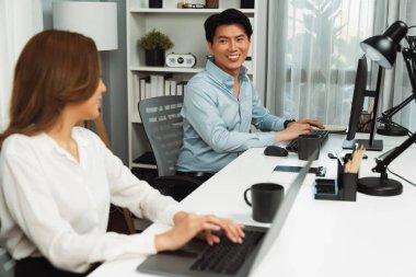 Gülümseyen Asyalı bir adam, yan görüntüdeki modern ofis çalışma masasında veri tabanını ararken günlük dizüstü bilgisayarla pazarlama raporu projesini planlarken kadın meslektaşıyla konuşuyor. İnfobahn.